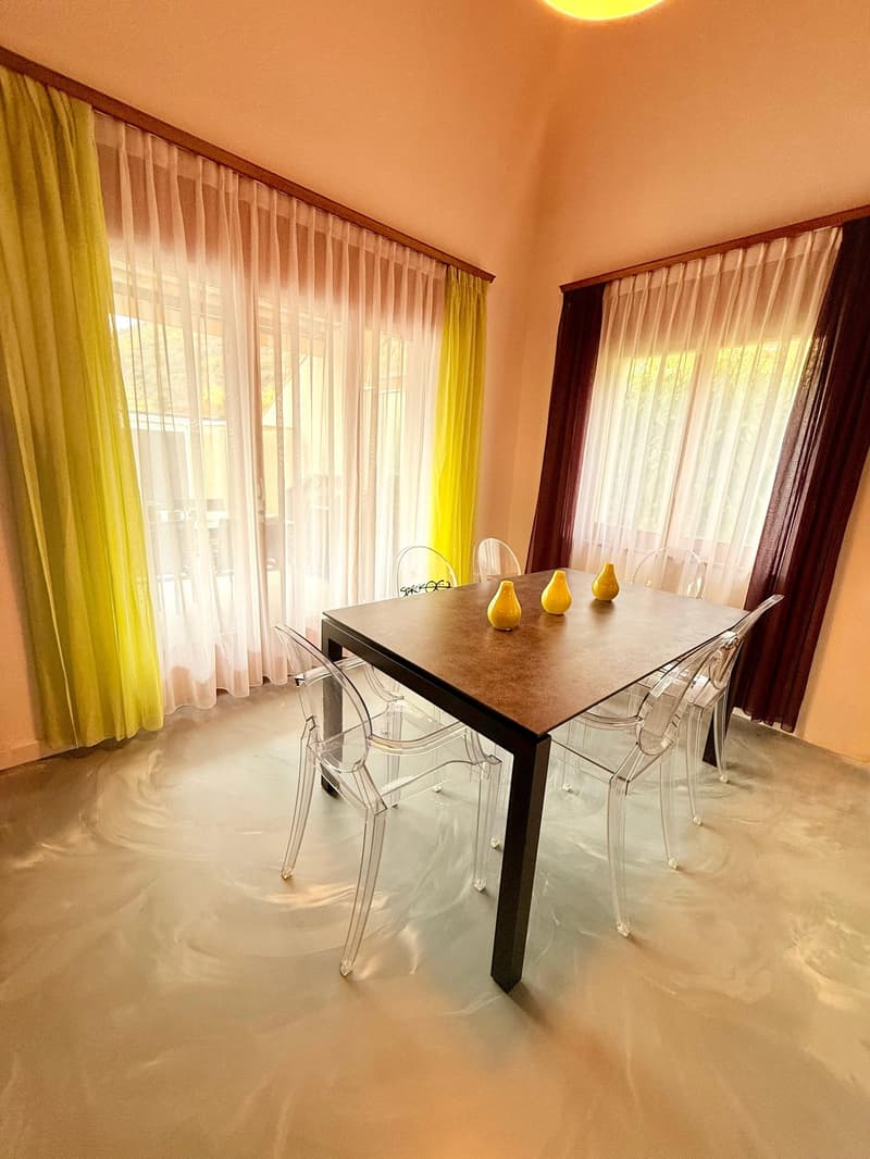Modern dining room, central dining table, transparent chairs, decorative vases, two windows with white and yellow curtains