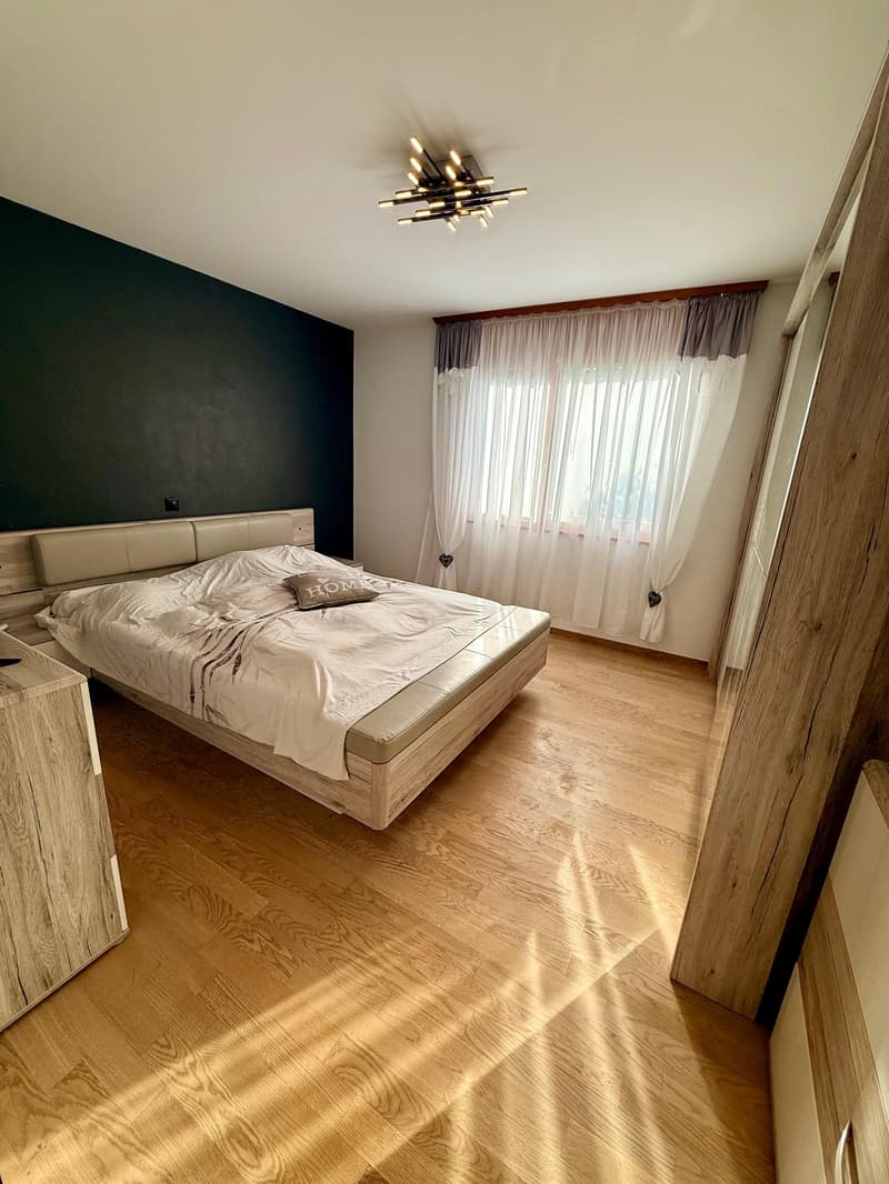 master bedroom with a king size bed, black walls, white window curtains, wooden floor, chandelier