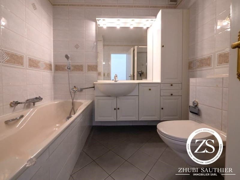 White tiled walls, bathtub, sink, toilet, mirror, cabinets, tiled floor, shower