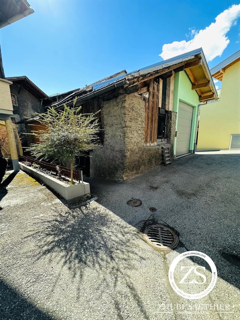 Single-story house with gravel driveway, garage, stone walls, concrete curb, small trees, sunny day