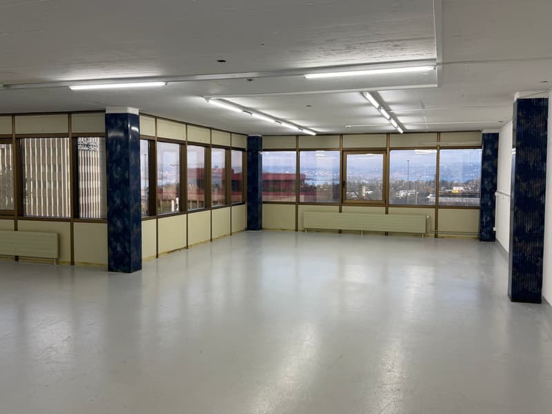 Empty room with large windows, white ceiling and floor, multiple pillars, multiple heaters.