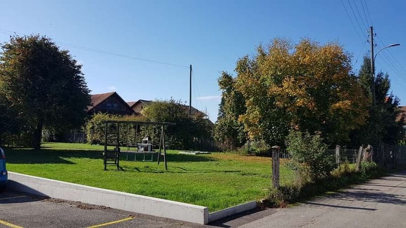 large open grass field with a playset, trees, street view