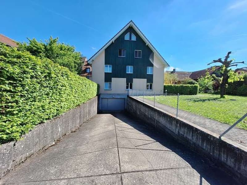 2 story house, green trim, open garage, hedges, concrete driveway