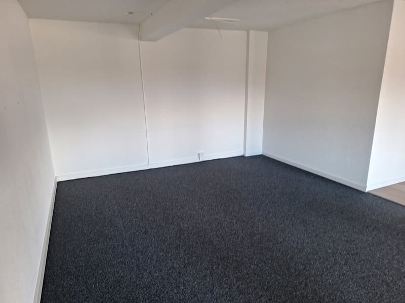 empty room with white walls, gray carpeted floor, and power outlet