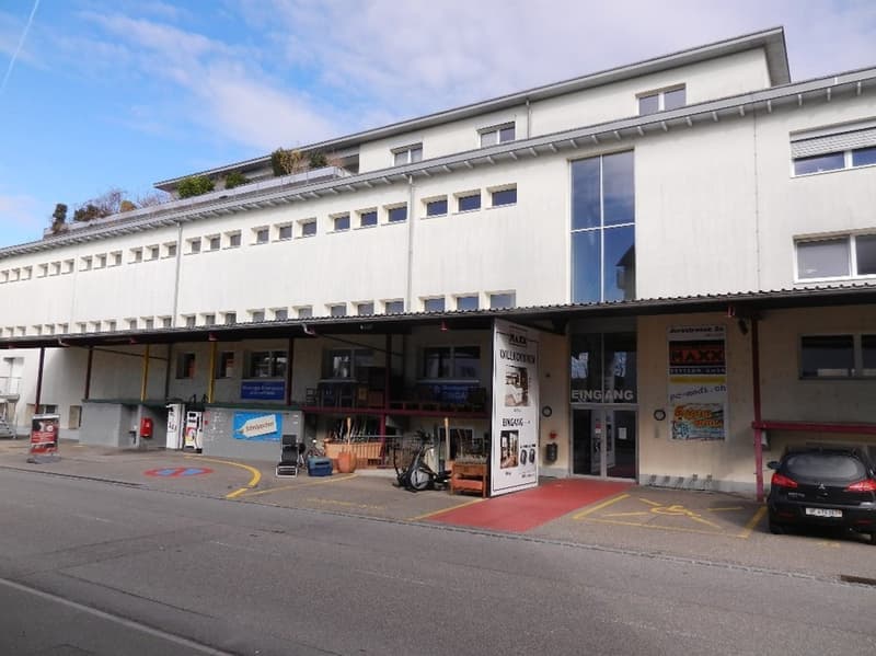Exterior of commercial building with glass windows, red carpet entrance, parked car, fire extinguisher