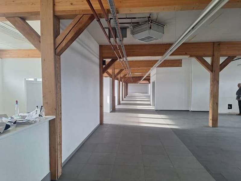 Wooden beams, grey tiled floor, white walls, empty, large windows, open space