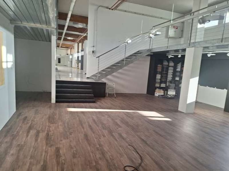 large empty room, wooden floor, staircase with metal railing, white walls, two doors at the end