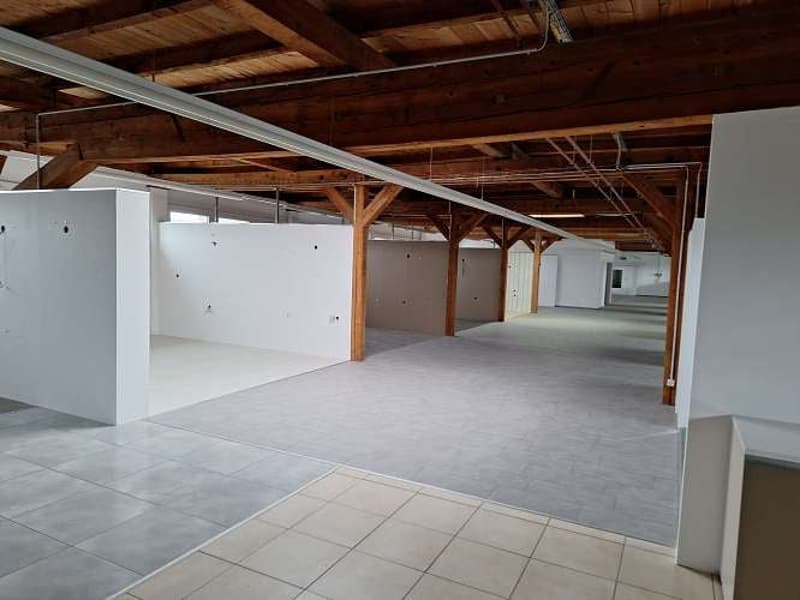 open space with gray and white tiled floor, wooden beams on the ceiling, white walls, and metal pipes