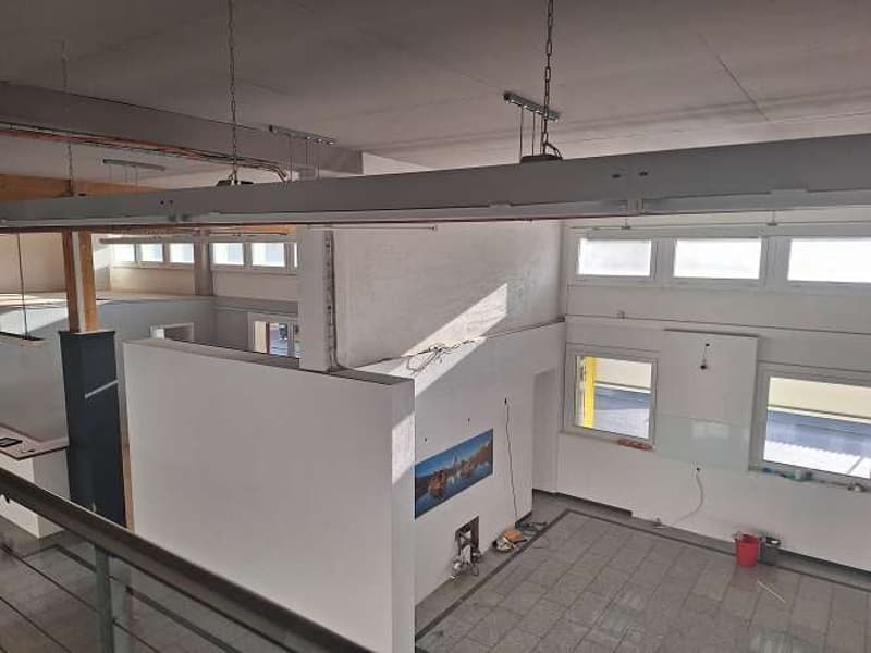 a blank room under construction, several windows, a balcony, picture on the wall, tiles floor, some buckets and wires on the floor.