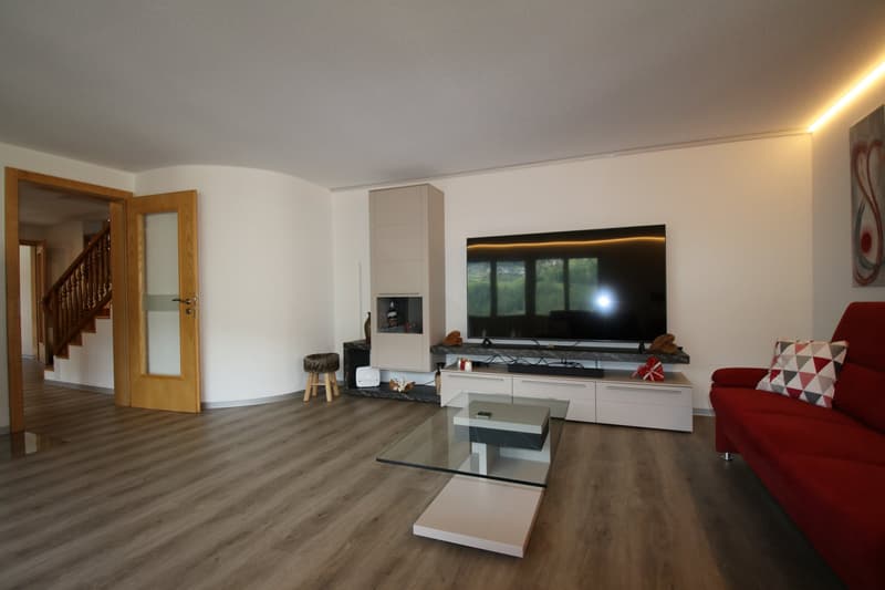 living room, fireplace, TV stand, large screen TV, glass coffee table, modern sofa, modern light fixtures, wooden floor, white wall, open door, staircase, stool