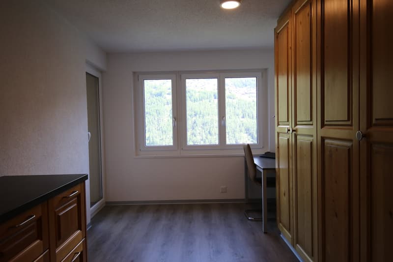 Empty room with white walls, wooden floor, a window, a desk, and wooden cabinets