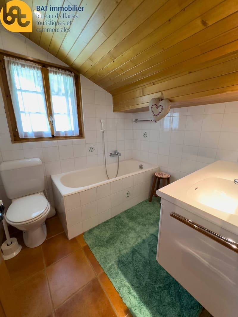Bathroom with wooden ceiling, white tiles, bathtub, toilet, vanity unit, and a private washing machine
