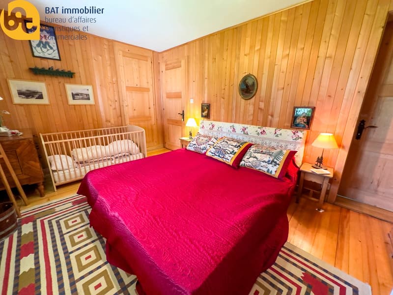Cozy bedroom with wooden walls, a large red bed, a crib, and decorative artwork on the walls. The room also features a fireplace.