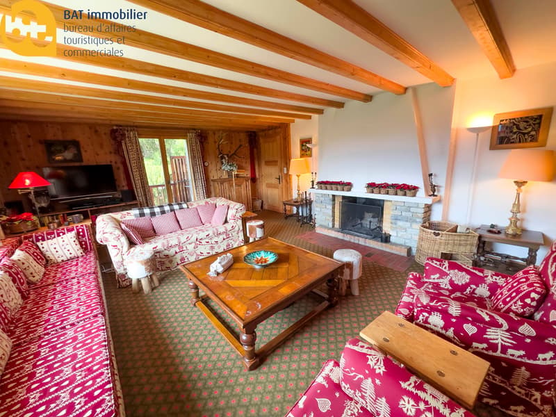 Cozy living room with wooden beamed ceiling, large fireplace, patterned sofas and chairs, wooden coffee table, and decorative accents like lamps and vases.