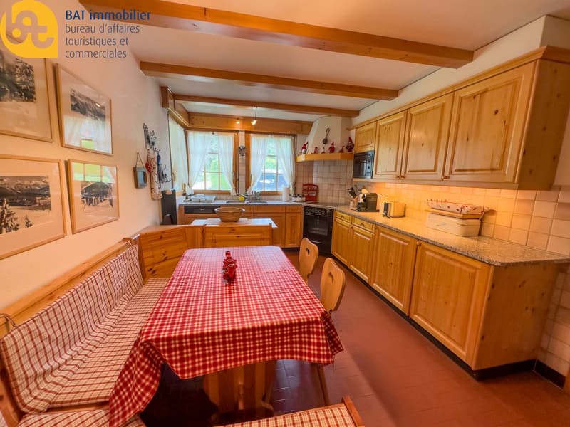 Spacious kitchen with wooden cabinets, tiled backsplash, granite countertops, dining table with checkered tablecloth, and various kitchen appliances including a dishwasher
