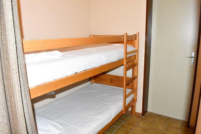 Wooden bunk bed with white bedding, tile flooring, and a curtain on the side