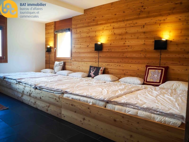 Spacious bedroom with wooden walls and floor, large bed with bedding, decorative pillows, and a fireplace