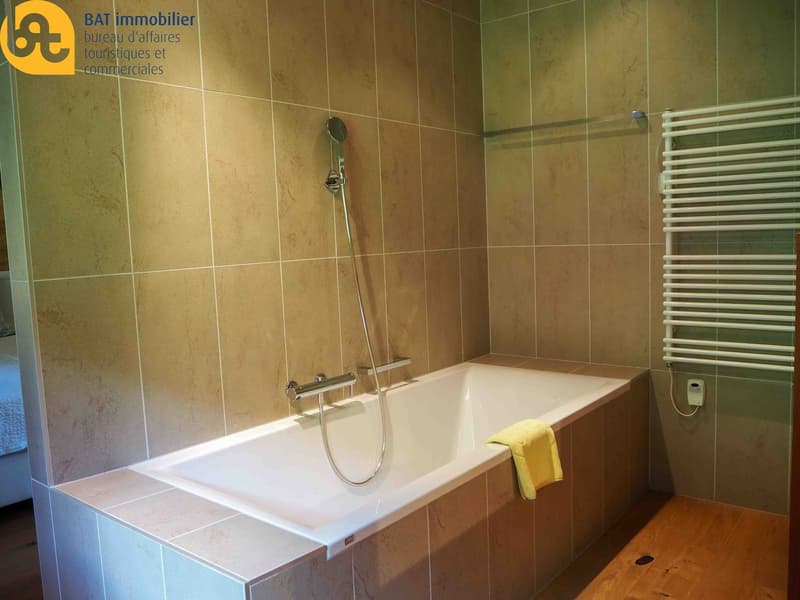 Spacious bathroom with beige tiled walls, a white bathtub, and a towel rack.
