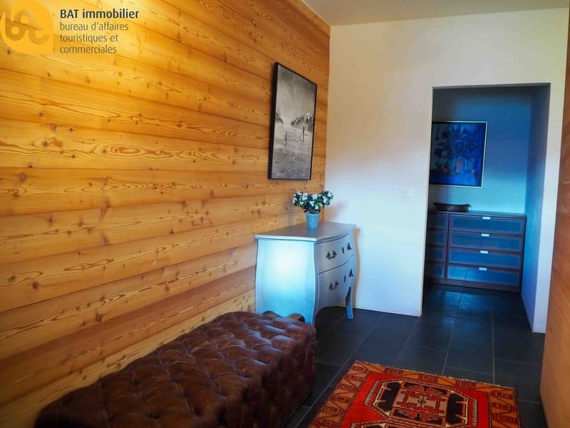The image shows a cozy interior with wooden walls, a tufted leather sofa, a blue vintage dresser, and artwork on the walls. There appears to be a fireplace visible in the room.
