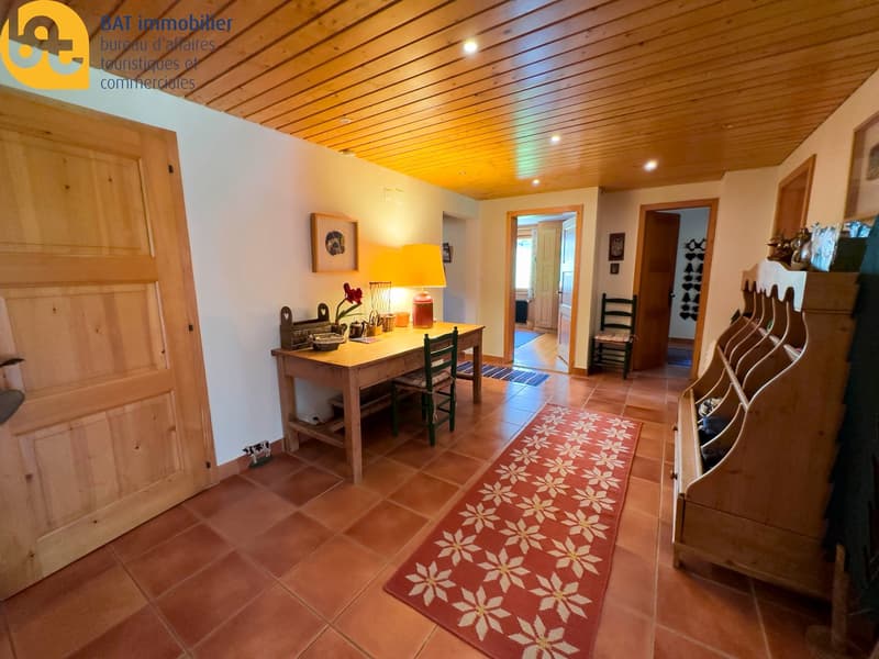 Cozy and rustic interior with wooden ceiling, tiled floor, wooden furniture, and a decorative rug. The room features a fireplace, creating a warm and inviting atmosphere.