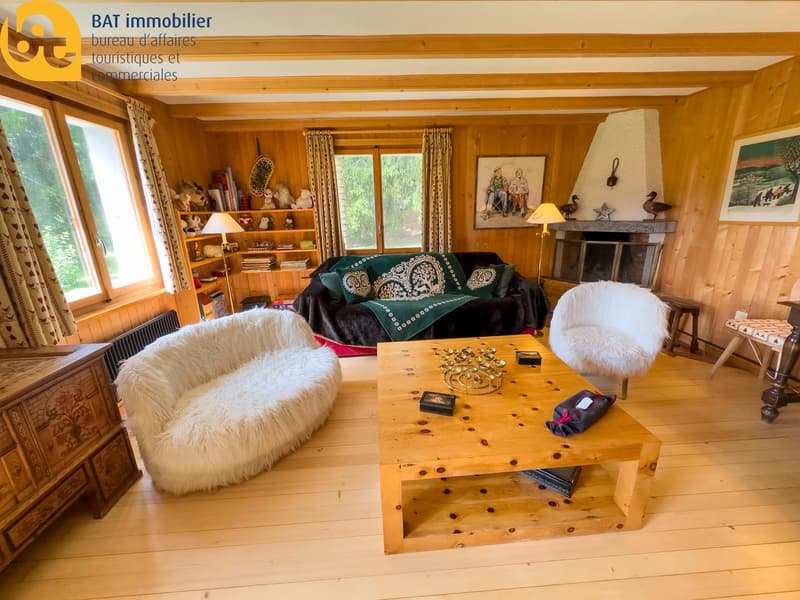 Cozy living room with wooden walls and ceiling, large windows, plush white furniture, wooden coffee table, and a fireplace