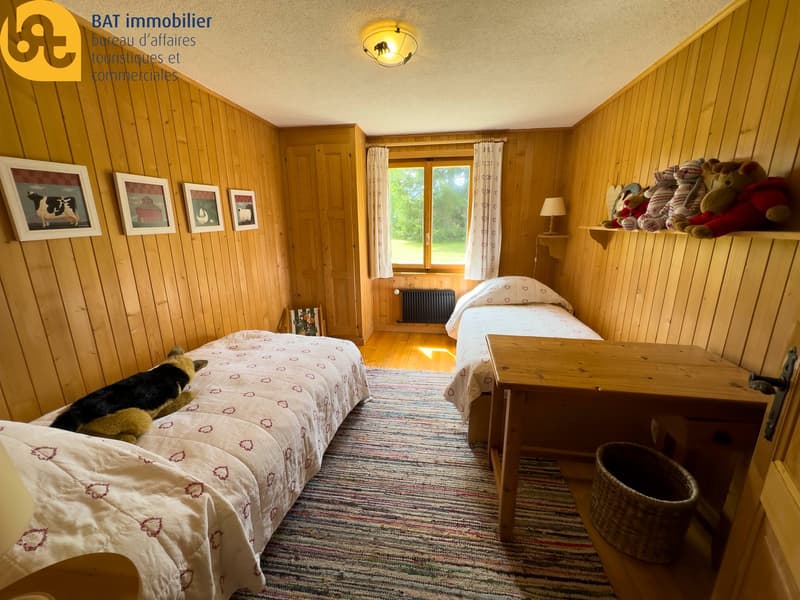 Cozy bedroom with wooden walls, two twin beds, wooden furniture, artwork on the walls, and a view through the window
