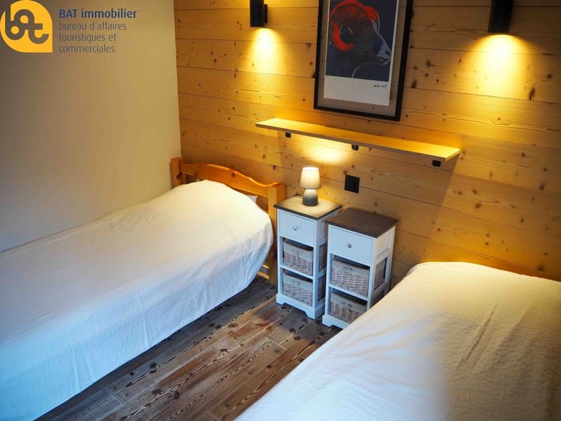 room with two beds, nightstands, baskets, wooden floor, wooden wall, mounted picture, wall lamp