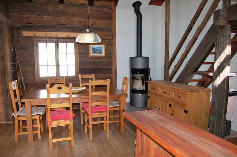 Rustic wooden cabin interior with a dining table and chairs, a wood-burning stove, and wooden furniture and decor elements.