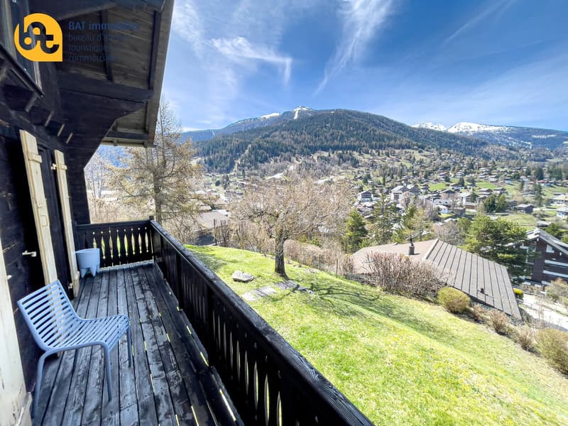 Balcony with a scenic view of a mountain town, surrounded by snow-capped peaks and lush greenery.