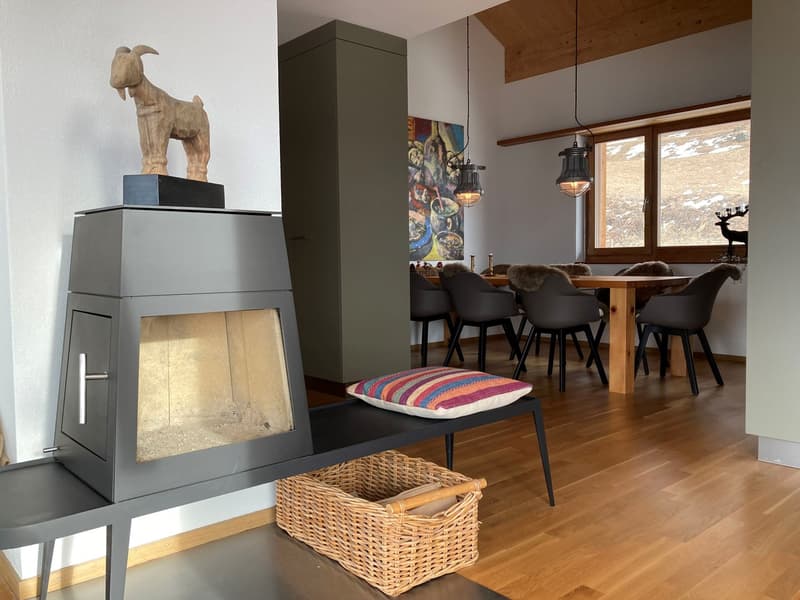 Fireplace with decorative goat, wooden table, wooden chairs, wicker basket, colorful pillow, metal bench, wooden flooring, wooden pendant lights