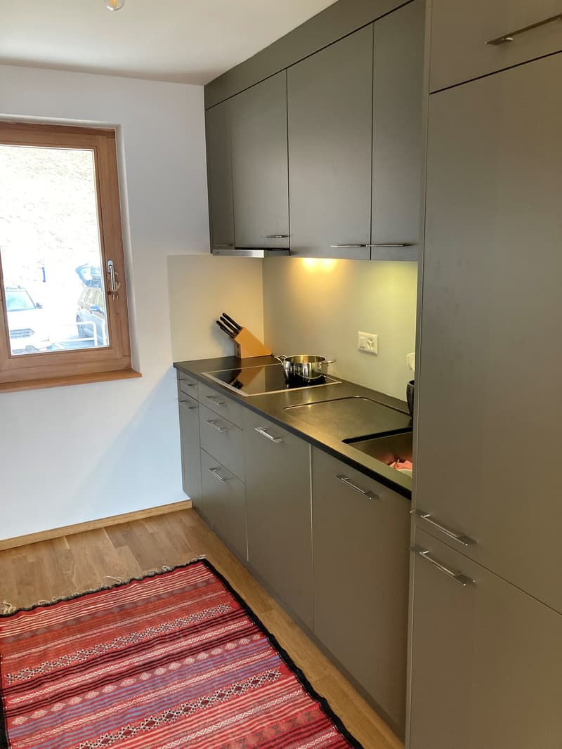 Modern kitchen with stainless steel countertops, gray cabinetry, a window with a wooden frame, a sink, and cooking utensils including a pot and knife block.