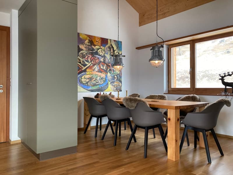 Dining room with wooden table, gray chairs, wooden floor, white walls, large window, painting, hanging lamps, wooden cabinet, deer statue