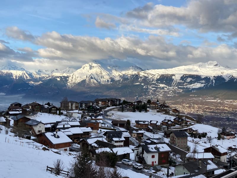 Mountain village with snow-covered houses, snowy mountains in the background, clear blue sky with clouds