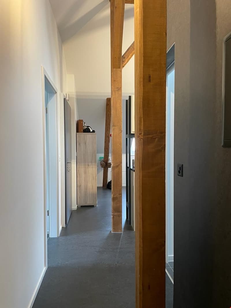 empty hallway with wooden support beams, white walls, grey flooring