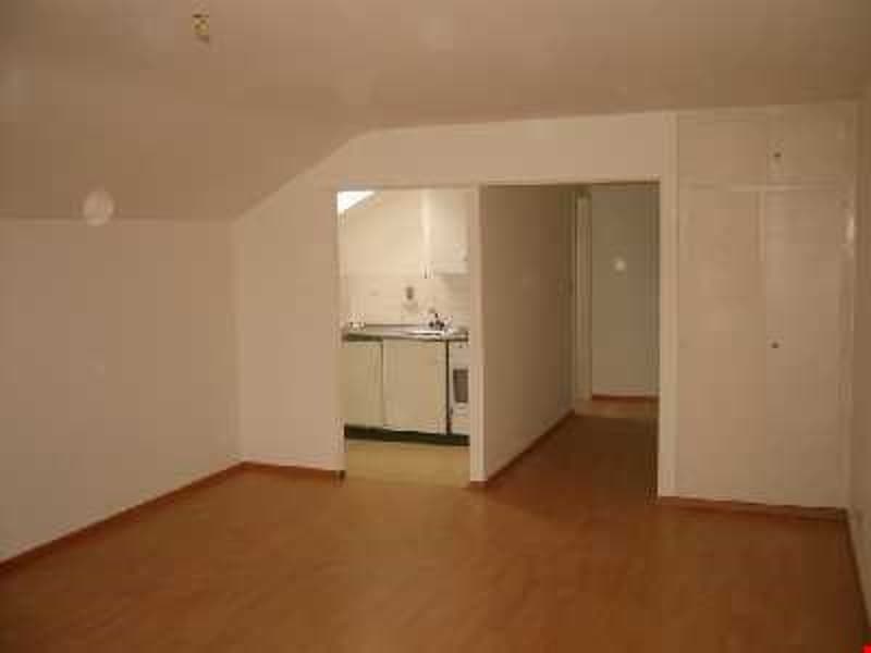 Empty room with wooden floor, white walls, kitchen area with sink and stove, two doors
