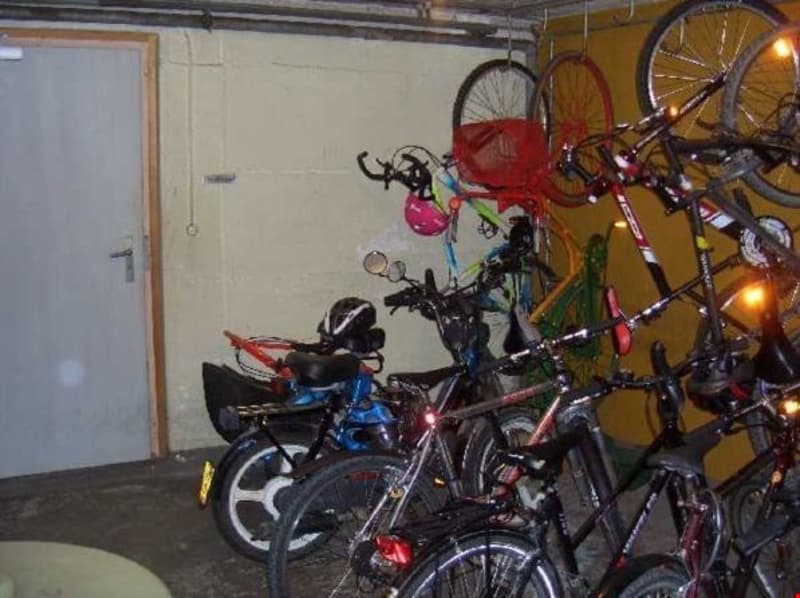 A room with a yellow wall, a white door, and a bicycle storage area with several bicycles and helmets