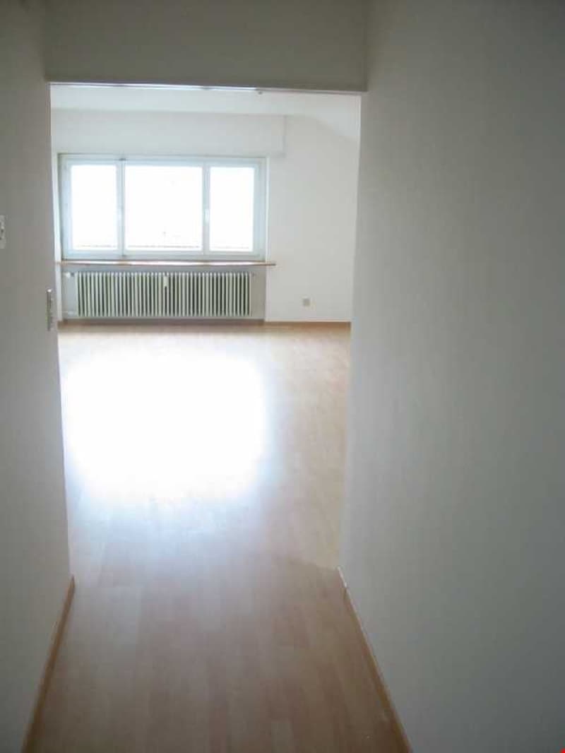 Empty room with wooden floor, white walls, large window, and a radiator.