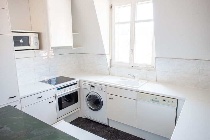 White kitchen with granite countertop, gas stove, white cabinets, dishwasher, washing machine, microwave, sink, window