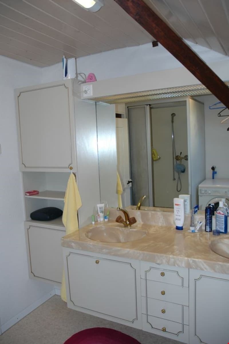 Bathroom with double sink, mirror, shower, washing machine, cabinets, and towels