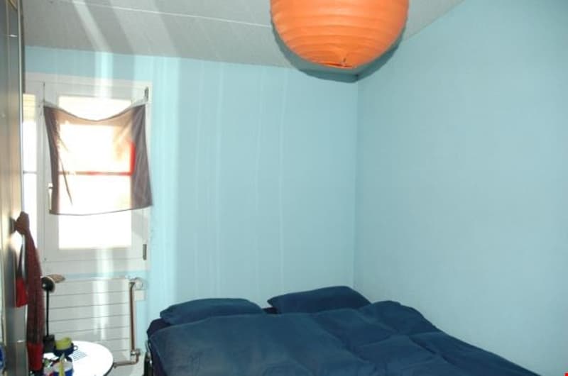 small bedroom with bed, blue walls, window, orange lamp