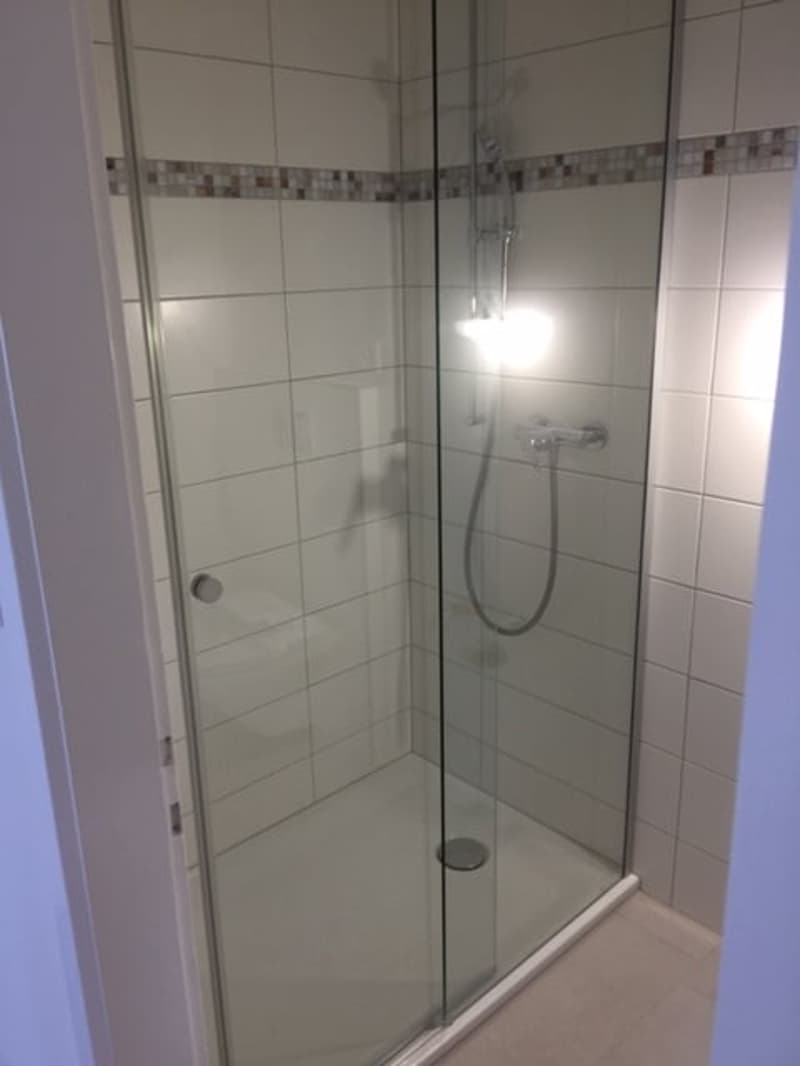 shower stall with glass door, tiled walls, shower head, drain