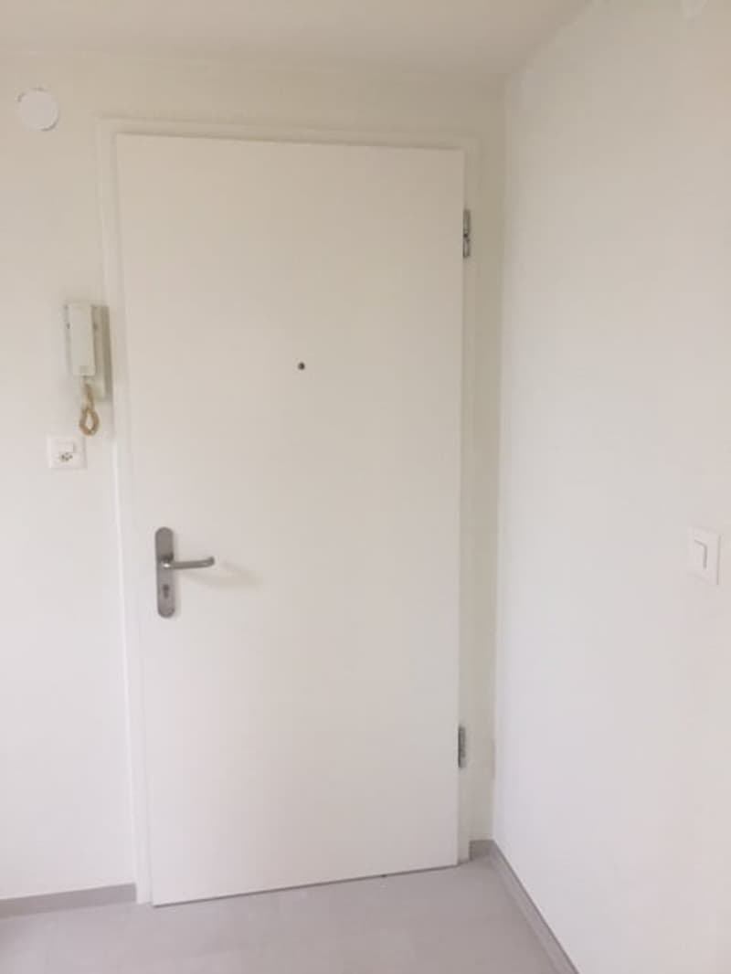 Empty room with white walls, white door, telephone, power outlet, and a small hole on the wall