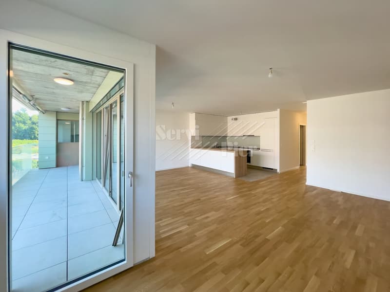 Spacious open-plan living area with hardwood flooring, large sliding glass doors leading to a balcony or terrace, and a modern kitchen with white cabinets and integrated appliances.