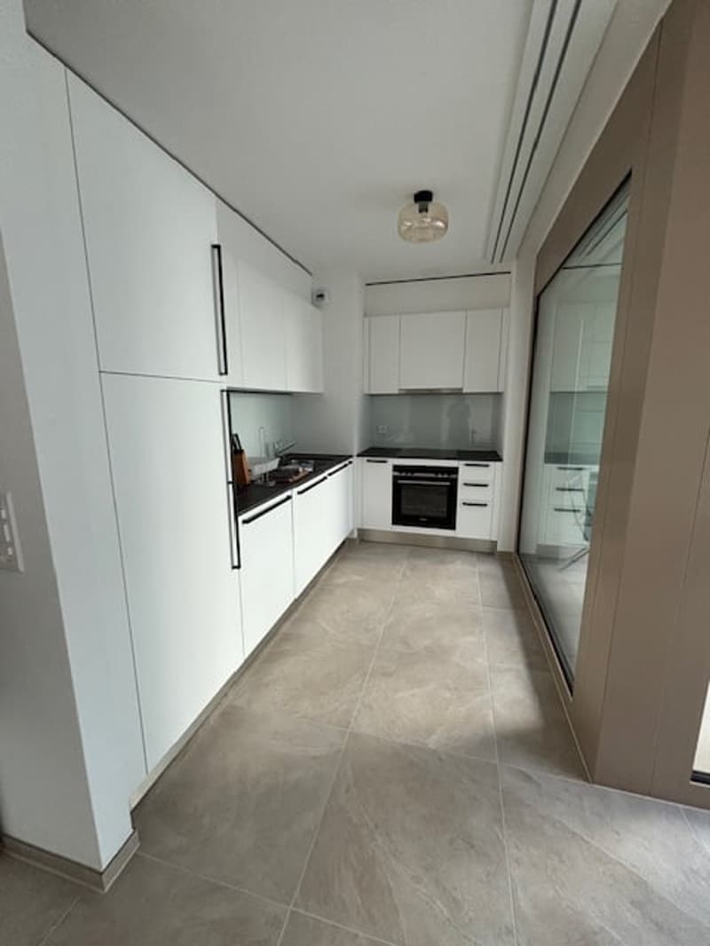 modern kitchen with white cabinets, tiled floor, black countertops, built-in oven, glass door
