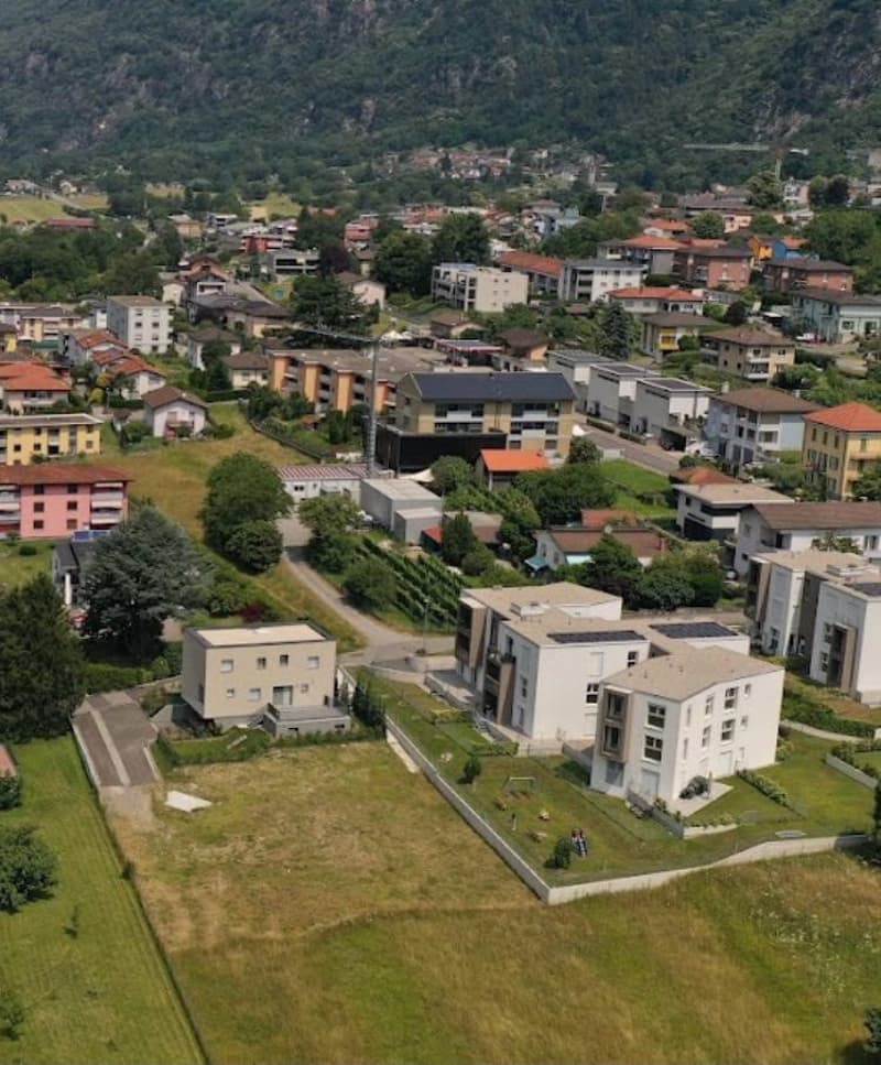This image shows a residential area in a mountainous region. The area is densely populated with multi-story apartment buildings and houses. The buildings have a mix of architectural styles and colors, with some having red tile roofs. The area is surrounde