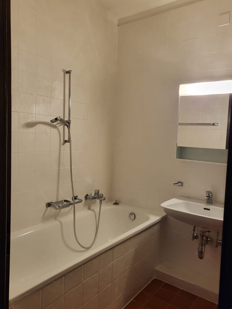 Bathroom with bathtub, sink, and shower. White tiled walls and floor.