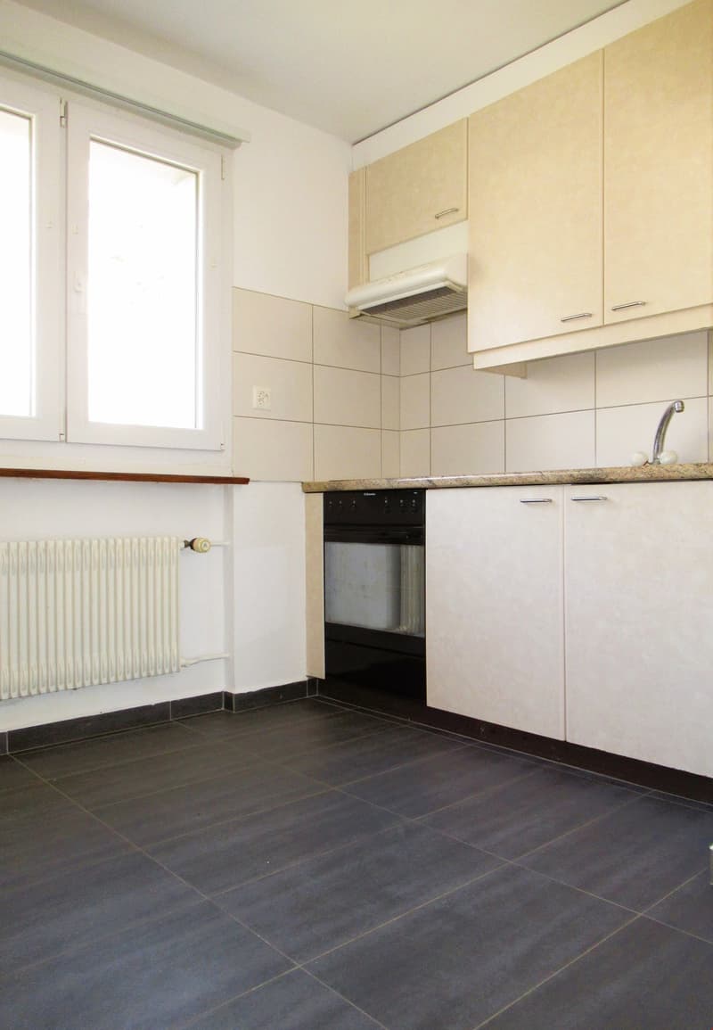 Empty kitchen with white tiles, wooden floor, white cabinets, white radiator, black oven, sink with faucet
