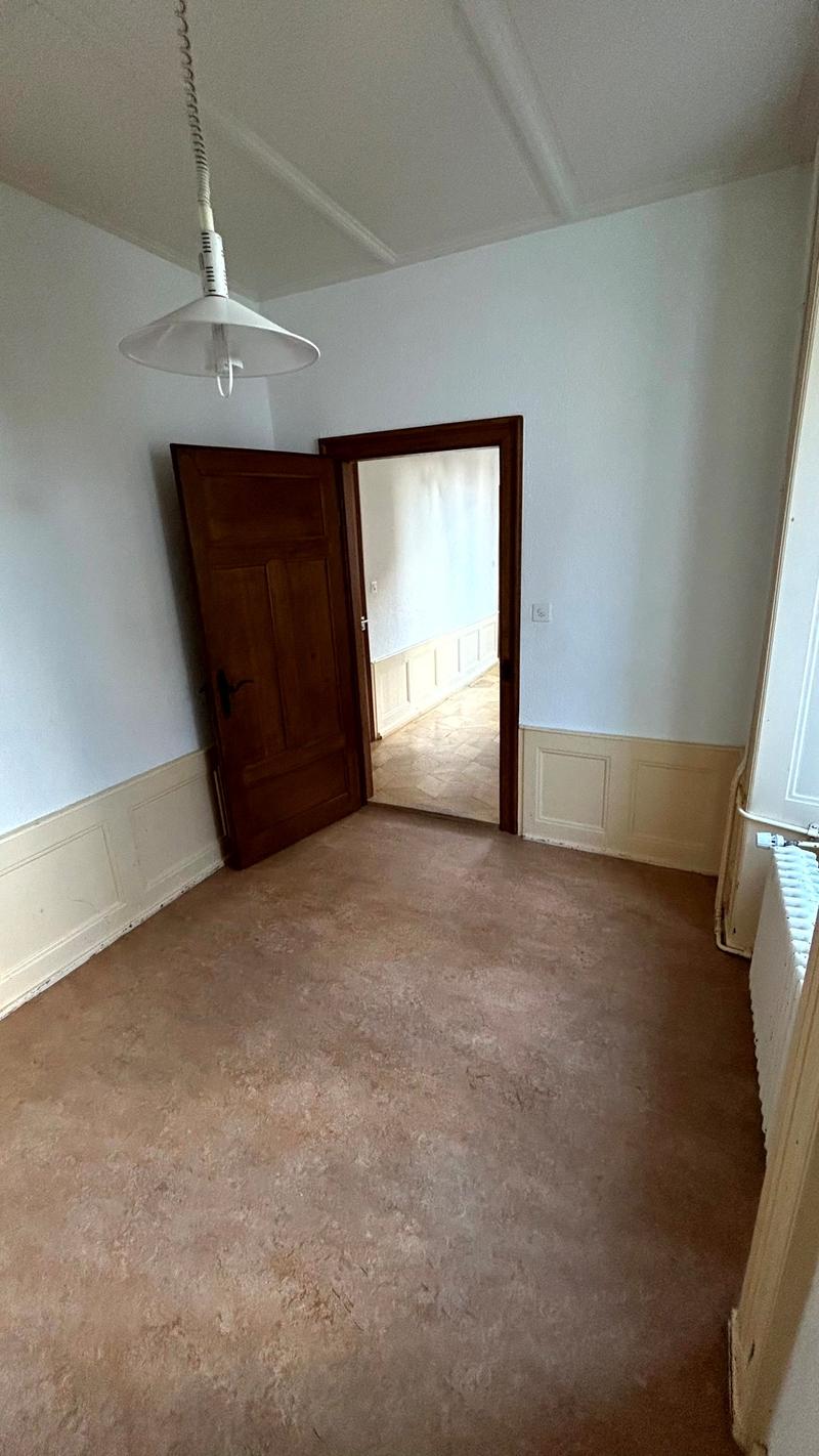 empty room, wood door, white walls, brown carpet, radiator, hallway