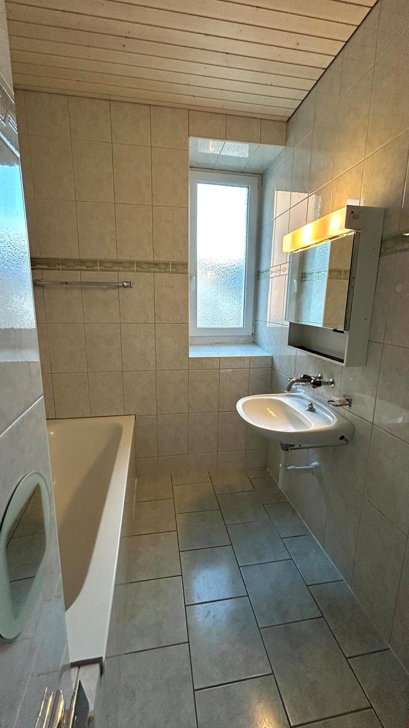 Bathroom includes white bathtub, white sink, mirror, wall lamp, and white ceramic tiles.