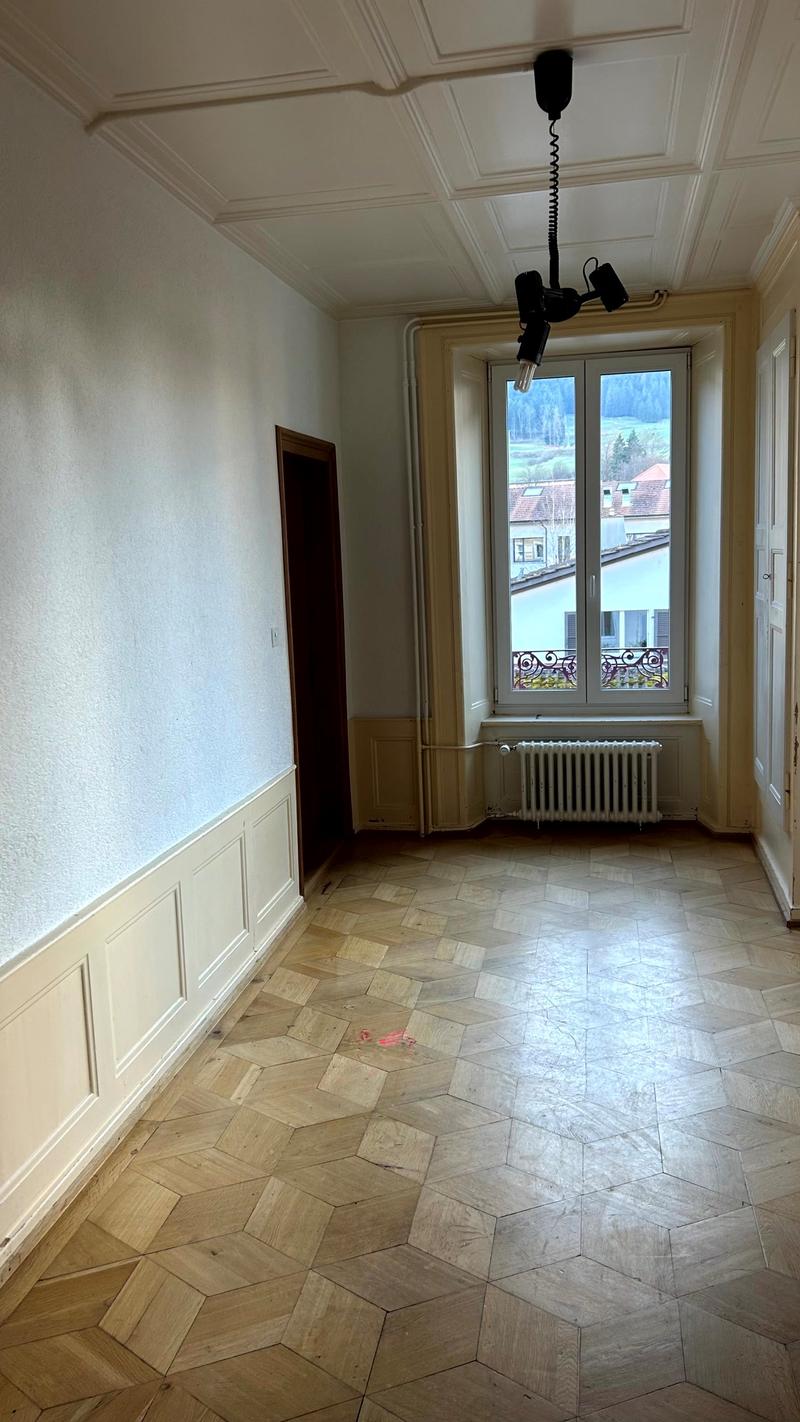 empty room with parquet floor, white walls, wooden door, white radiator, glass window, ceiling lamp